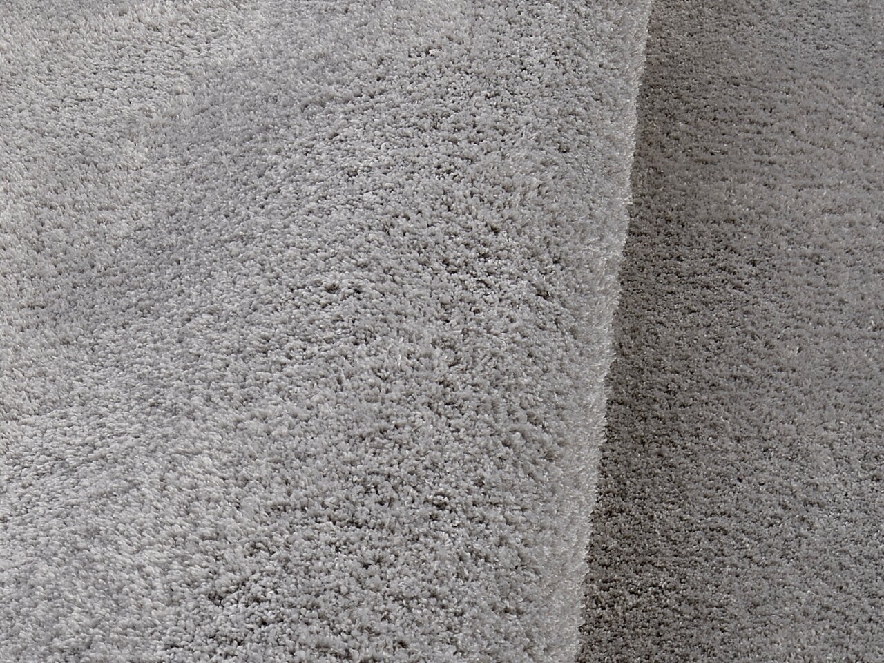 Nahaufnahme eines weichen, grauen Teppichs mit flauschiger Textur, perspektivisch von der Seite aufgenommen.