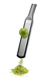 Feinreibe RAFINO in seitlicher Perspektive mit einer Limette, die über die Reibe gerieben wird, und Limettenschale, die darunter fällt.