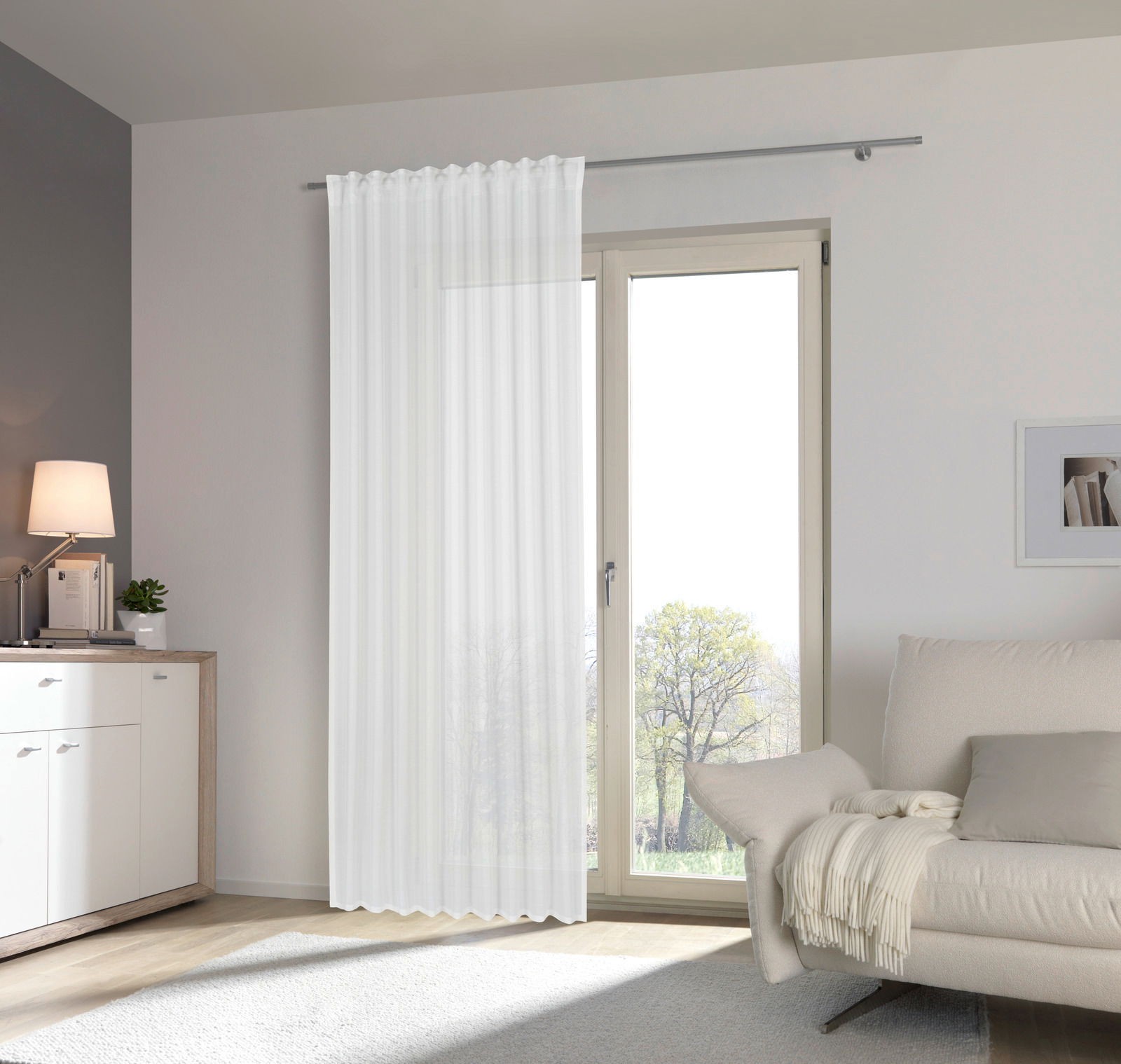 Moderner, weißer Fertigvorhang Esposa vor einer großen Fensterfront in einem hellen Wohnzimmer, seitliche Perspektive.