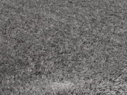 Grauer Hochflor-Teppich in Nahaufnahme, der die weiche und flauschige Textur des Materials zeigt.