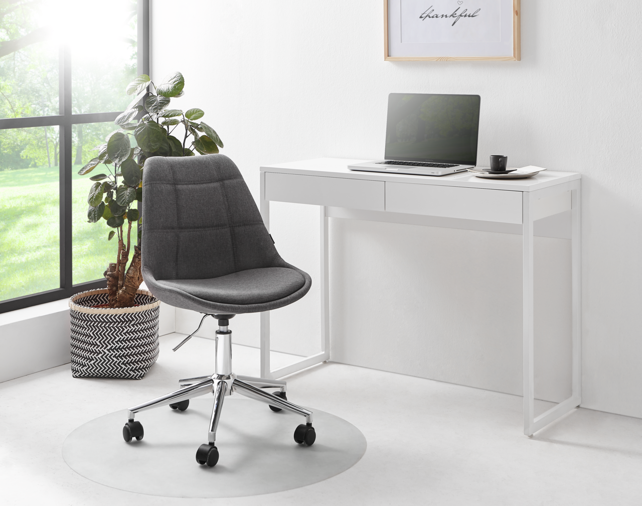 Moderner weißer Schreibtisch mit zwei Schubladen, darauf ein Laptop und eine Tasse, daneben ein grauer Bürostuhl auf Rollen. Perspektive von vorne.