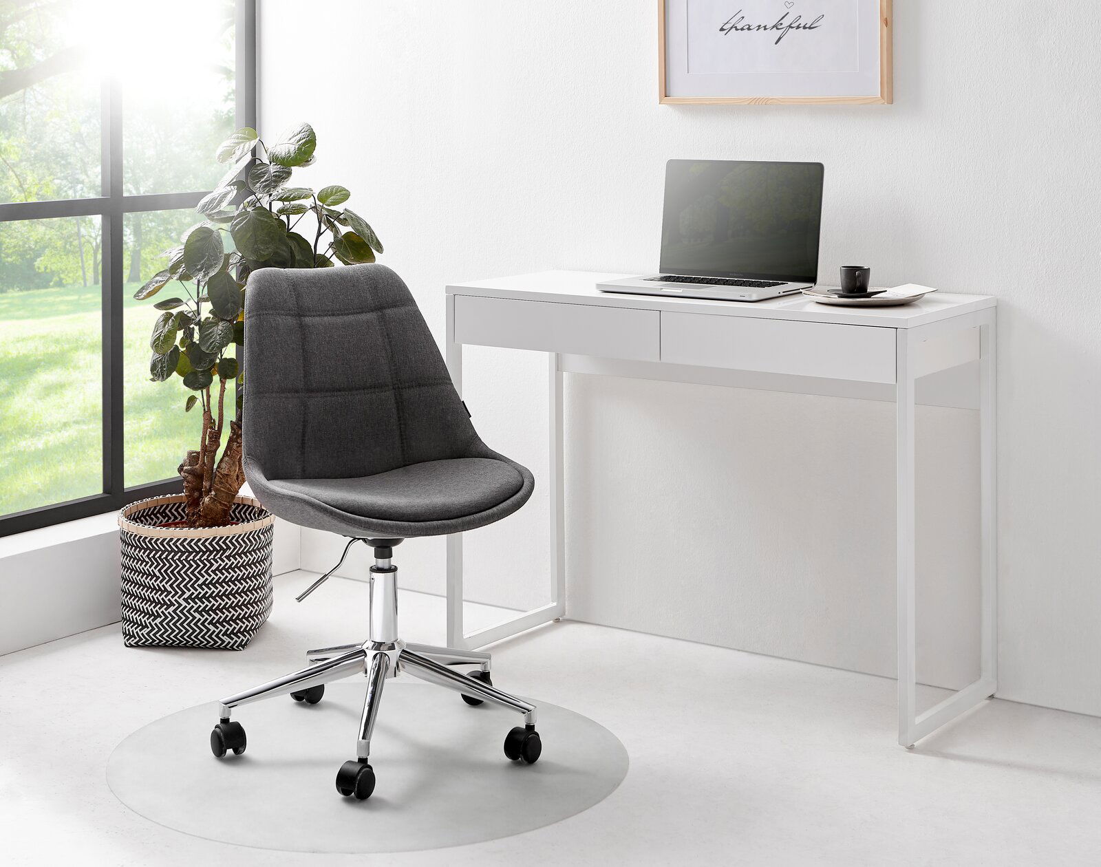 Moderner weißer Schreibtisch mit zwei Schubladen, darauf ein Laptop und eine Tasse, daneben ein grauer Bürostuhl auf Rollen. Perspektive von vorne.