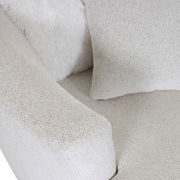 Nahaufnahme eines beigen Sessels mit weicher Textur, Kissen und flauschiger Decke, von oben betrachtet.