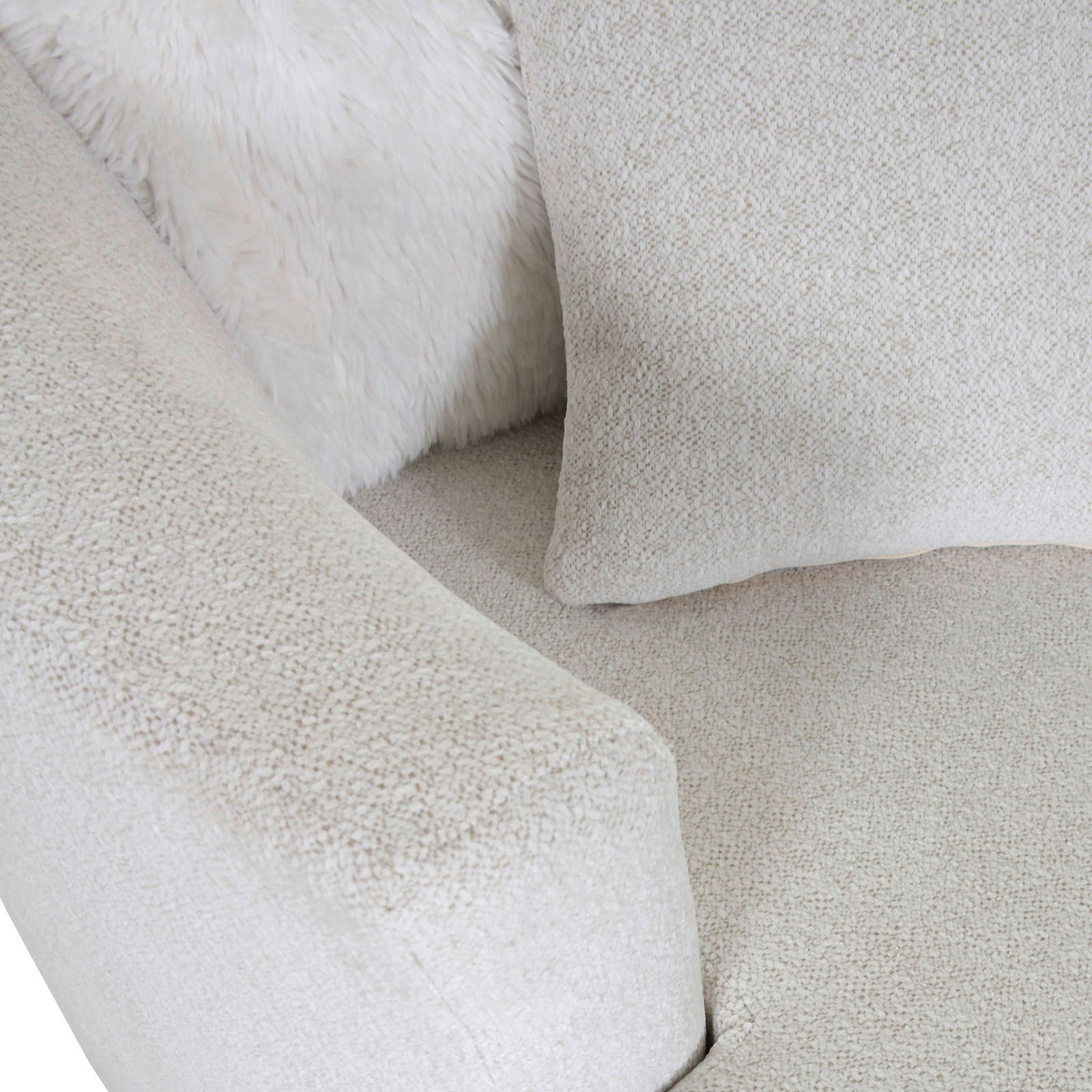 Nahaufnahme eines beigen Sessels mit weicher Textur, Kissen und flauschiger Decke, von oben betrachtet.