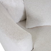 Nahaufnahme eines beigen Sessels mit weicher Textur, Kissen und flauschiger Decke, von oben betrachtet.