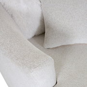Nahaufnahme eines beigen Sessels mit weicher Textur, Kissen und flauschiger Decke, von oben betrachtet.