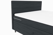 Seitliche Ansicht eines modernen Boxspringbetts mit dunklem Stoffbezug und weißer Matratze.