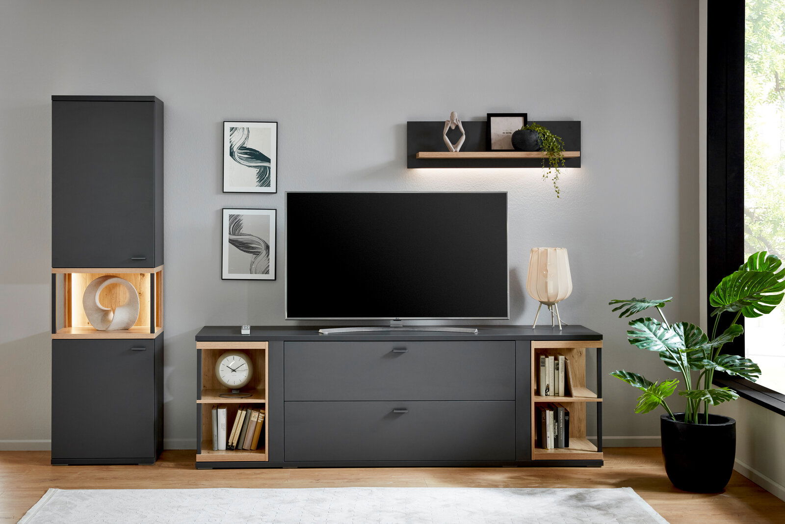 Moderne Wohnwand mit dunklen Schränken, dekorativen Regalen und einem großen Fernseher in einer stilvollen Wohnzimmerumgebung, frontal betrachtet.