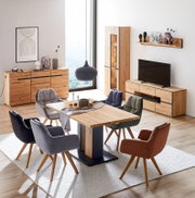 Schuine frontaanzicht van een modern eet- en woonkamerinterieur met eikenhouten eettafel en dressoirs, tv-meubel en vitrinekast met zwarte accenten, omringd door gestoffeerde stoelen in verschillende kleuren en een hanglamp.