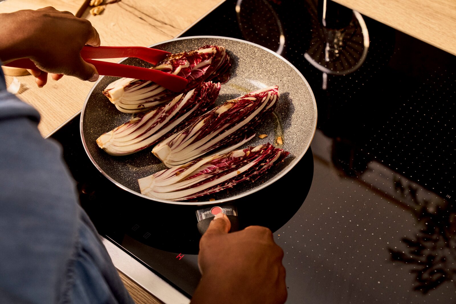 Person brät Radicchio in einer BALLARINI Bratpfanne BOLOGNA GRANITIUM CERAMIC auf einem Herd, von oben betrachtet.