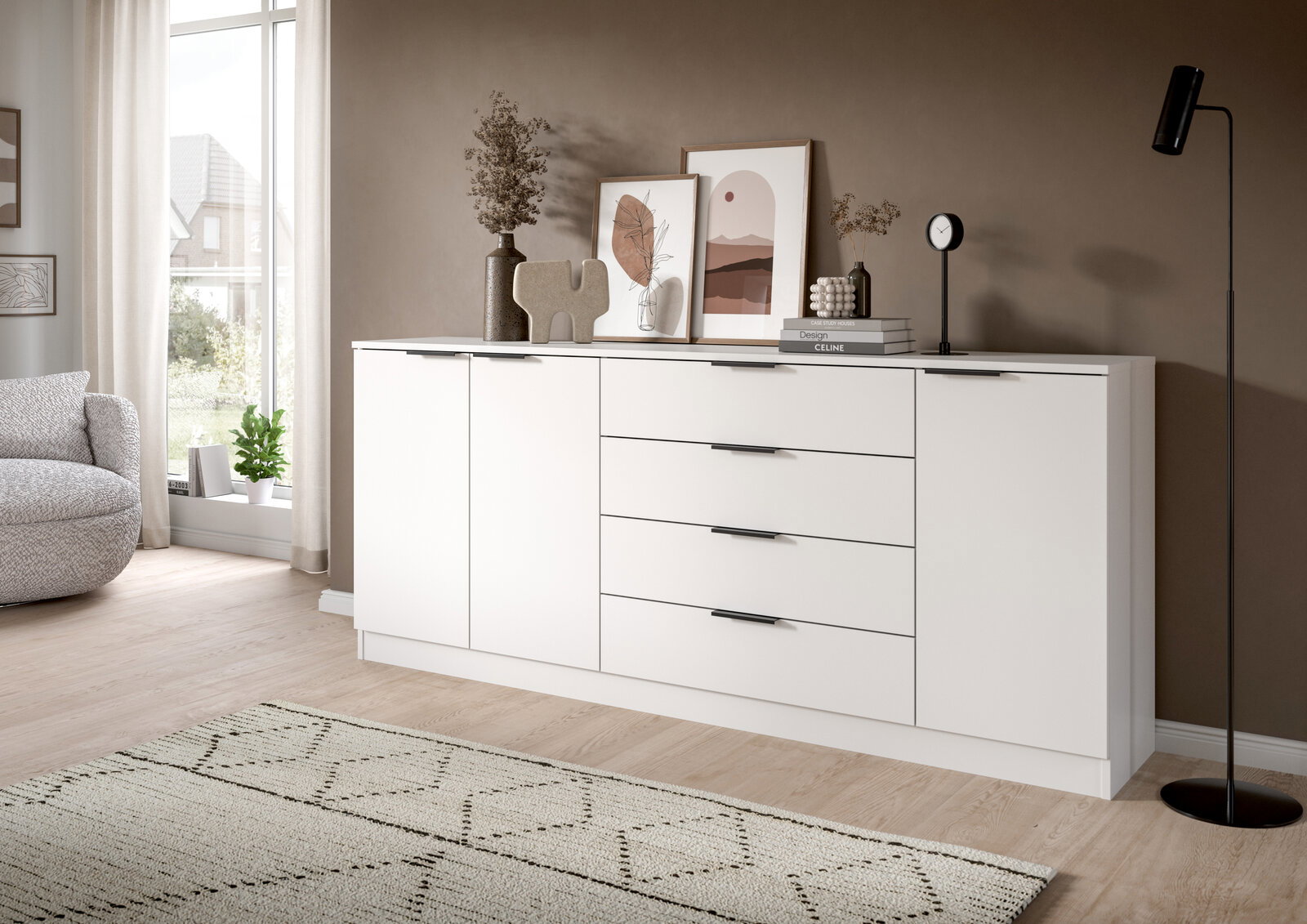 Moderne weiße Sideboard-Kommode mit zwei Türen und vier Schubladen, schwarzen Griffleisten und Deko auf der Ablage in einem hellen Wohnzimmer; Ansicht schräg von vorn.