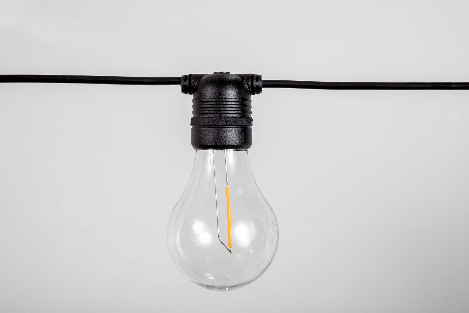 Transparente LED-Glühbirne an schwarzer Lichterkette vor hellem Hintergrund, Frontalansicht