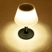 Zonne-tafellamp van 28 cm in zwart, die oplicht in een donkere omgeving, gezien van bovenaf.
