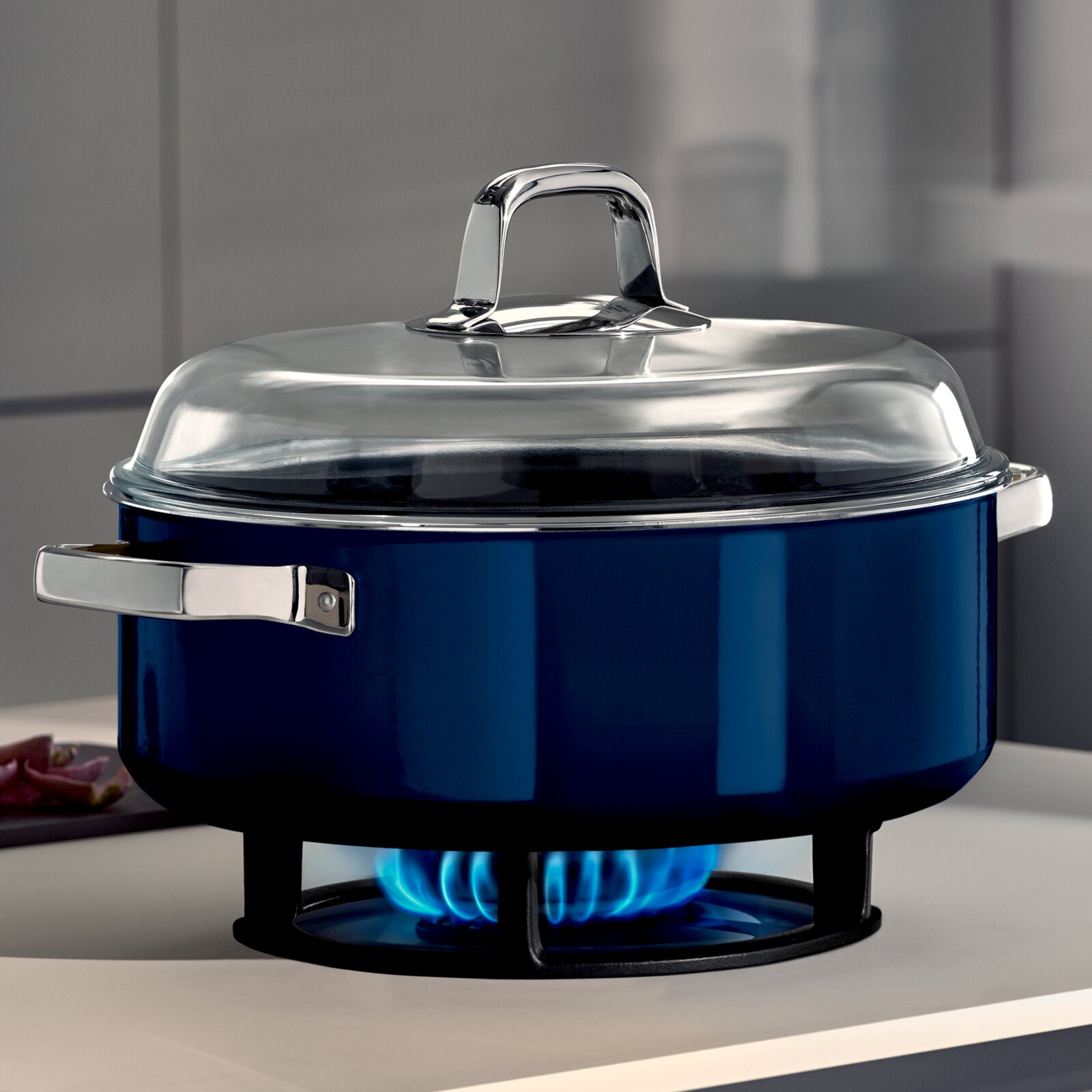 Blauwe braadpan met glazen deksel, zijaanzicht, op een fornuis met een blauwe vlam