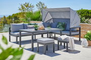 Modernes Dining-Lounge-Set auf einer Terrasse mit Blick auf die Natur, bestehend aus einem Tisch, einer Eckbank mit Sonnenschutz und zwei Hockern, dekoriert mit Kissen und Pflanzen.