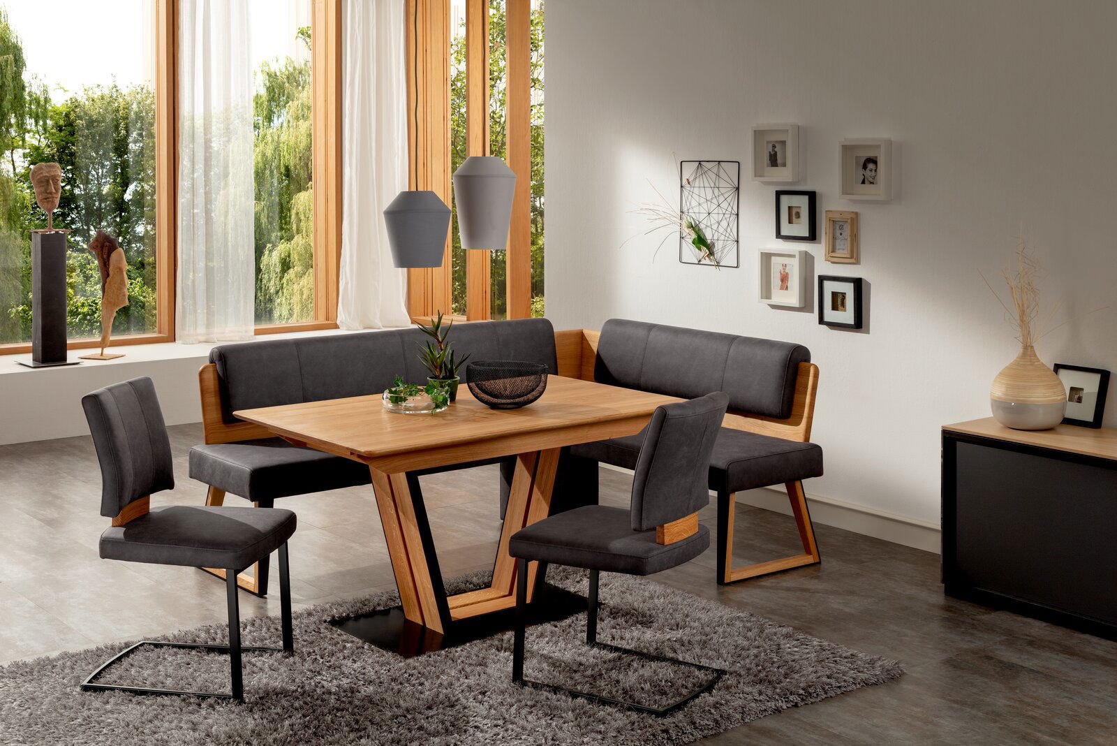 Moderne Esszimmer-Einrichtung mit Holztisch, Eckbank und Freischwinger-Stühlen in einem hellen Raum mit großen Fenstern, von schräg vorne betrachtet.