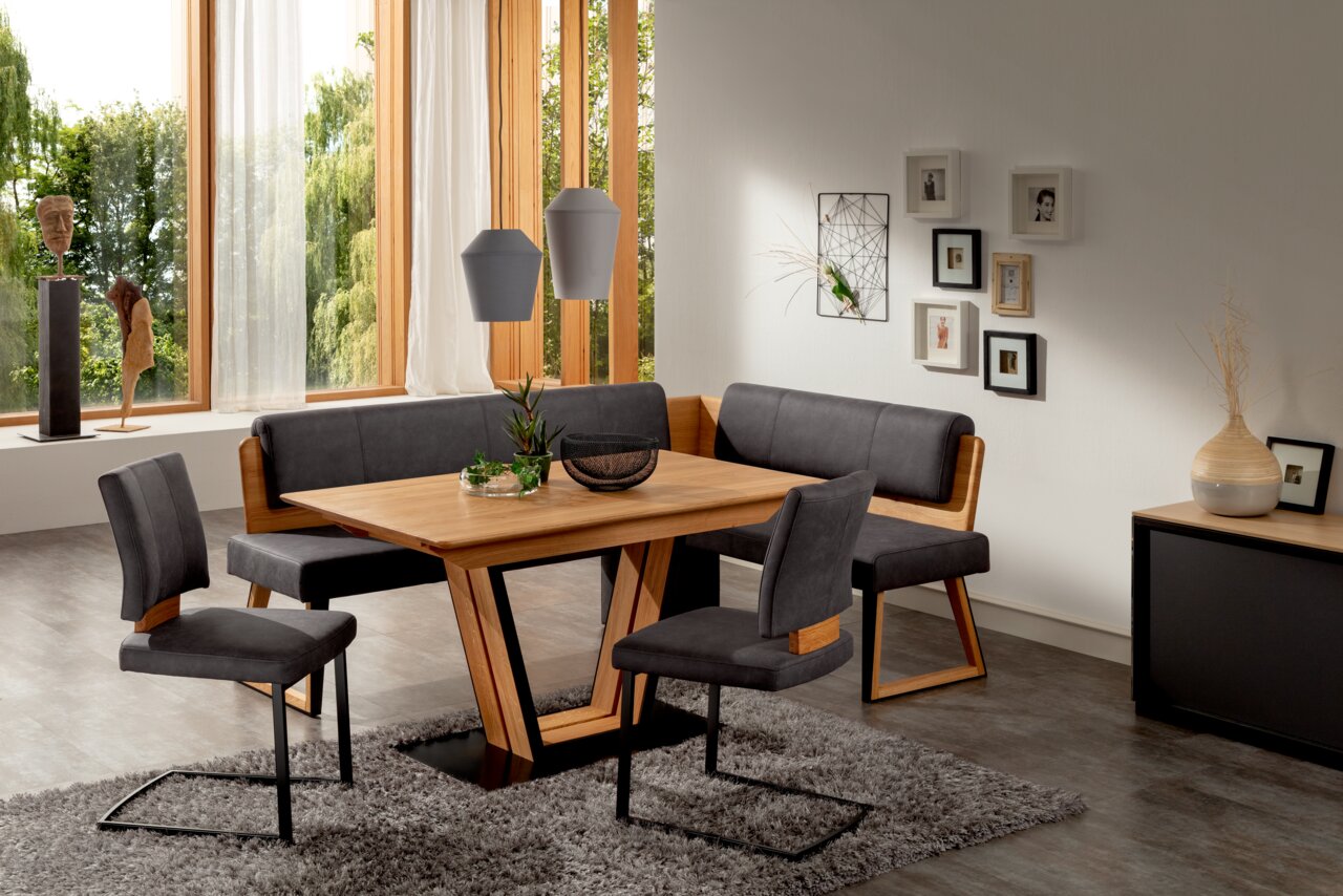 Een moderne eetkamerinrichting met een houten tafel, een hoekbank en zweefstoelen in een lichte ruimte met grote ramen, gezien vanuit een schuine hoek aan de voorkant.