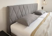 Graues Boxspringbett mit gestepptem Kopfteil, seitliche Perspektive