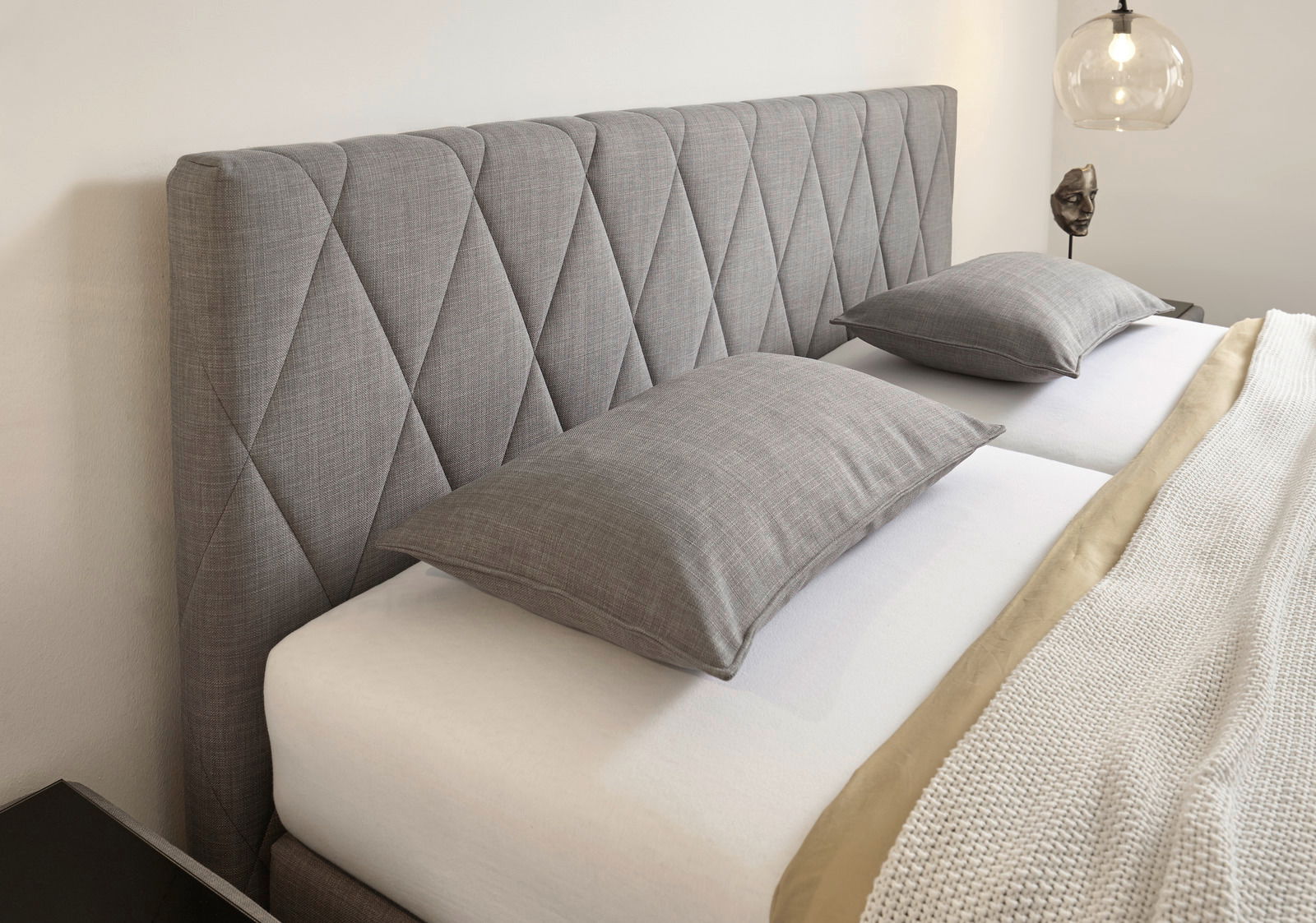 Graues Boxspringbett mit gestepptem Kopfteil, seitliche Perspektive