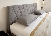 Graues Boxspringbett mit gestepptem Kopfteil, seitliche Perspektive