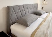 Graues Boxspringbett mit gestepptem Kopfteil, seitliche Perspektive