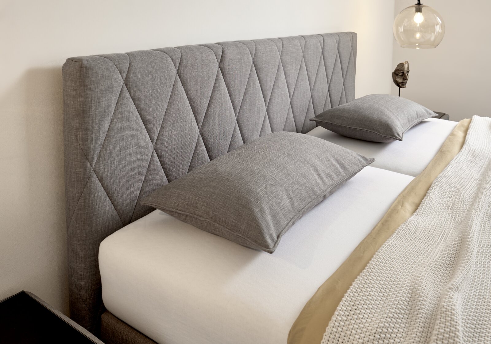 Graues Boxspringbett mit gestepptem Kopfteil, seitliche Perspektive