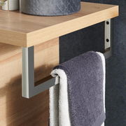 Nahaufnahme eines modernen Handtuchhalters aus Metall, montiert an einem Holzregal, mit einem grauen Handtuch. Perspektive von der Seite.