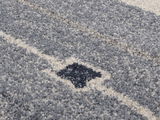 Nahaufnahme eines grauen und cremefarbenen Frisé-Teppichs mit geometrischem Muster.