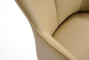 Close-up van een beige leren fauteuil, met de nadruk op de stiksels en de armleuning, gezien van bovenaf.