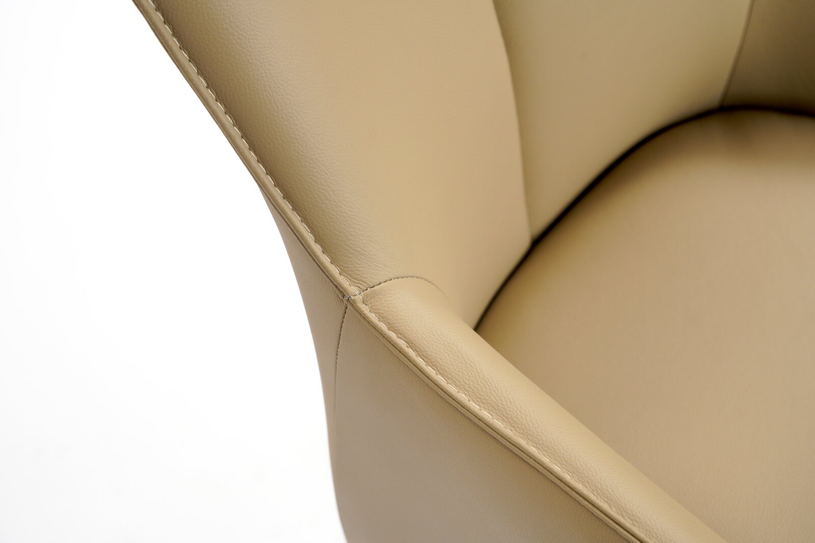 Close-up van een beige leren fauteuil, met de nadruk op de stiksels en de armleuning, gezien van bovenaf.