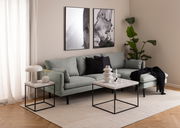 Moderner Couchtisch mit Marmorplatte und schwarzem Metallgestell, seitliche Perspektive im Wohnzimmer mit grünem Sofa und Dekoration.