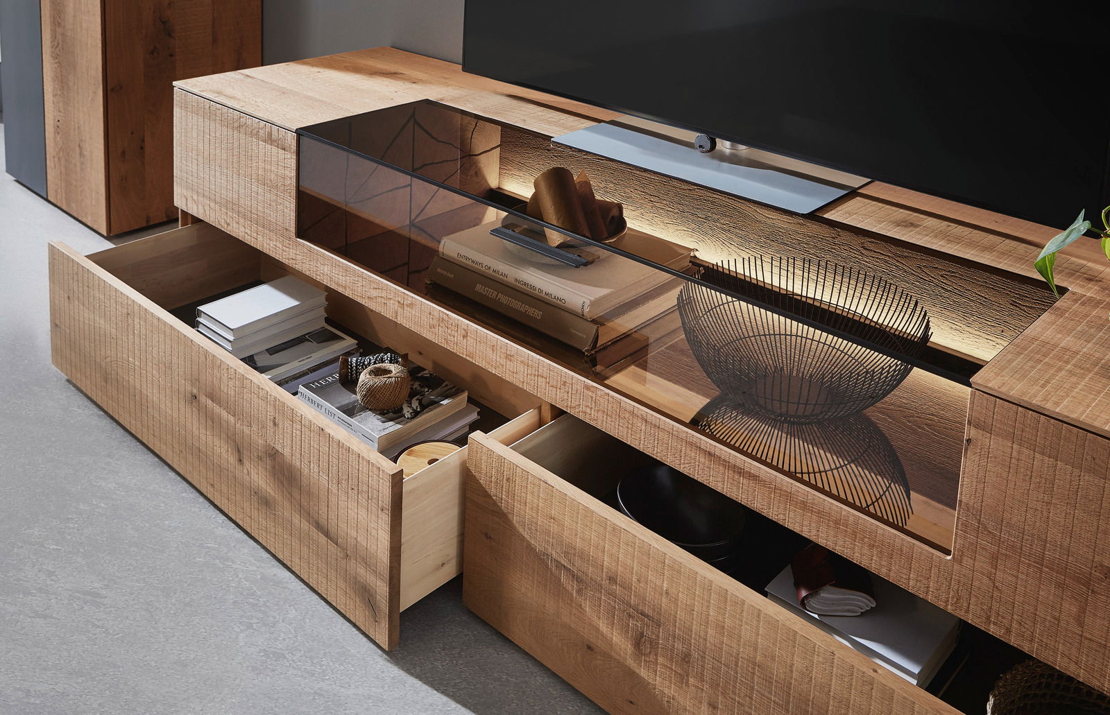 Nahaufnahme einer modernen Wandkombination aus Holz mit offenen Schubladen, die Bücher und Dekorationsgegenstände zeigen. Die Perspektive ist von schräg oben.