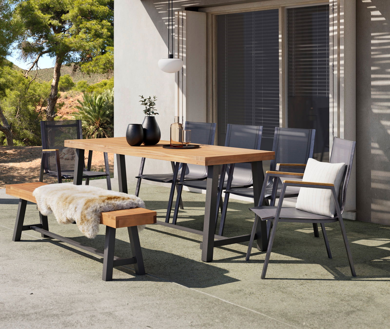 Ambia Garden Gartentisch SPLITWORK Moderner Gartentisch aus Holz mit Metallgestell, umgeben von Stühlen und einer Bank, auf einer Terrasse mit Blick auf einen Garten.