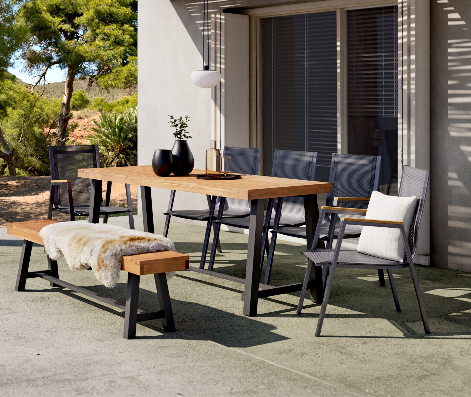 Ambia Garden Gartentisch SPLITWORK Moderner Gartentisch aus Holz mit Metallgestell, umgeben von Stühlen und einer Bank, auf einer Terrasse mit Blick auf einen Garten.