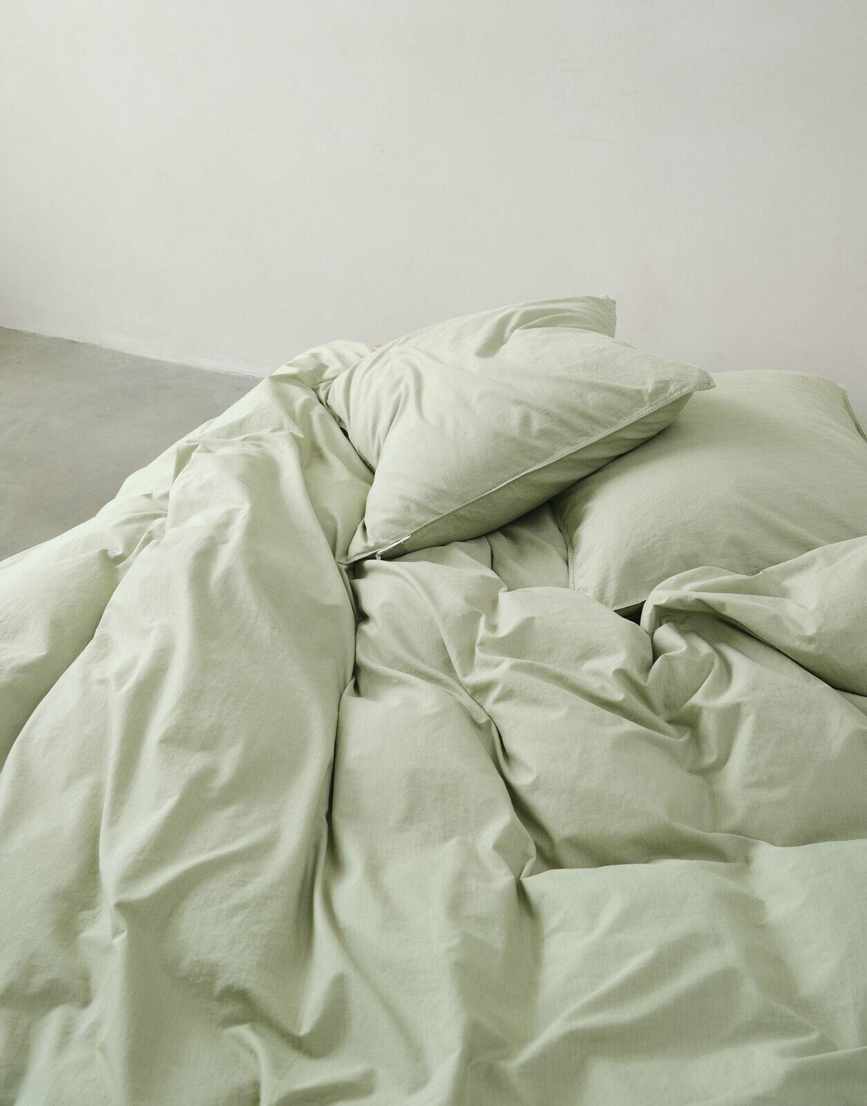 Grüne Bettwäsche 155x220cm aus der Vogelperspektive auf einem Bett arrangiert.