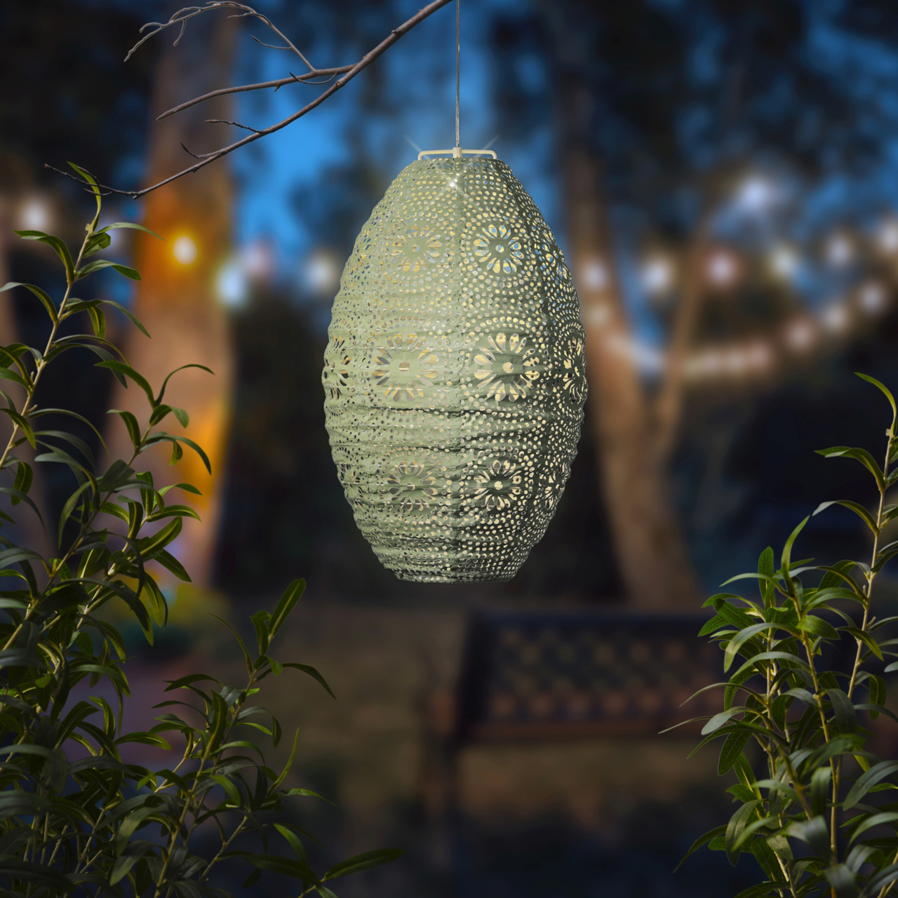 Hängende Solar Laterne mit filigranem Muster, beleuchtet in einem Garten bei Dämmerung, seitliche Perspektive