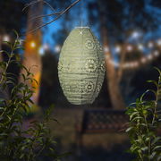 Hängende Solar Laterne mit filigranem Muster, beleuchtet in einem Garten bei Dämmerung, seitliche Perspektive