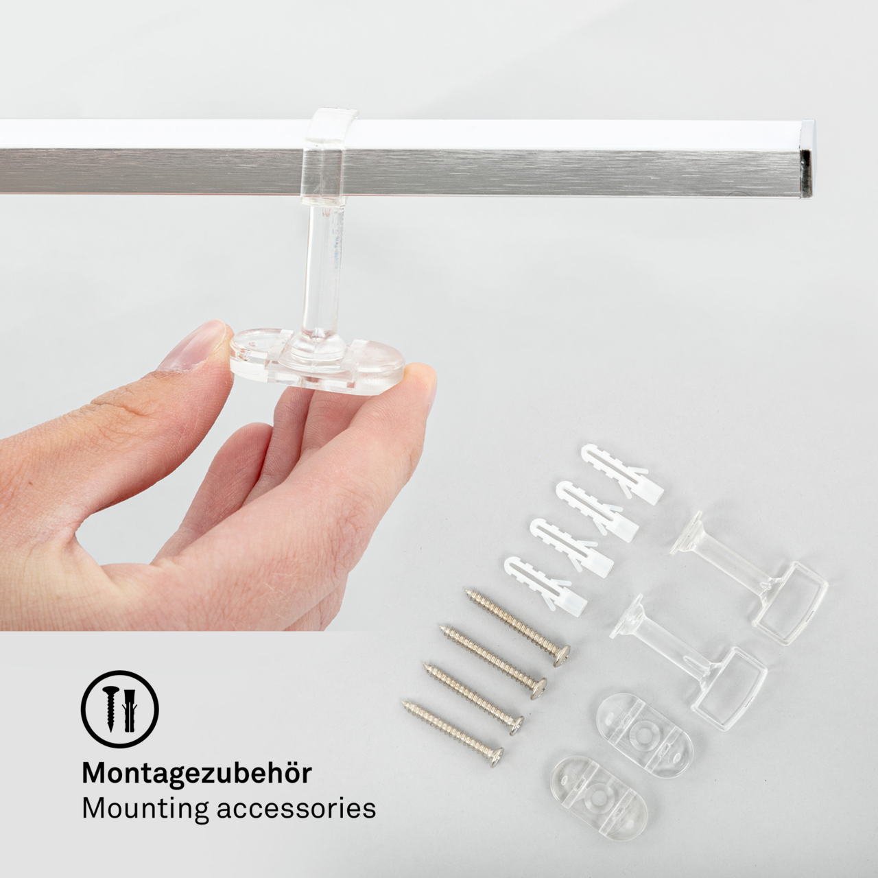 Montagezubehör für LED-Deckenleuchte, Nahaufnahme von Hand, die ein transparentes Befestigungselement hält, mit Schrauben und Dübeln im Hintergrund.