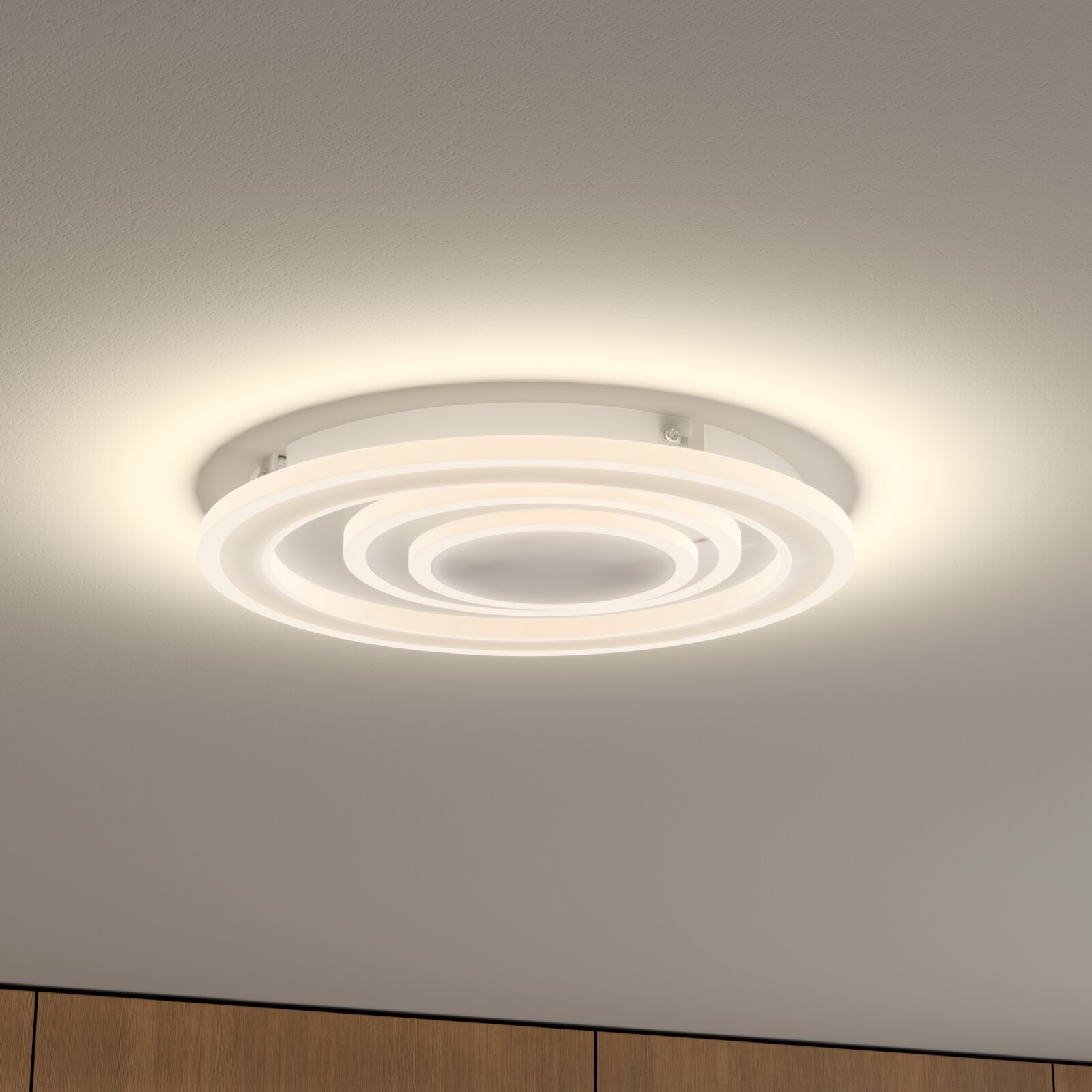 Weiße, runde LED-Deckenleuchte mit konzentrischen Leuchtringen an der Zimmerdecke, warmweiß leuchtend, Perspektive von unten schräg nach oben