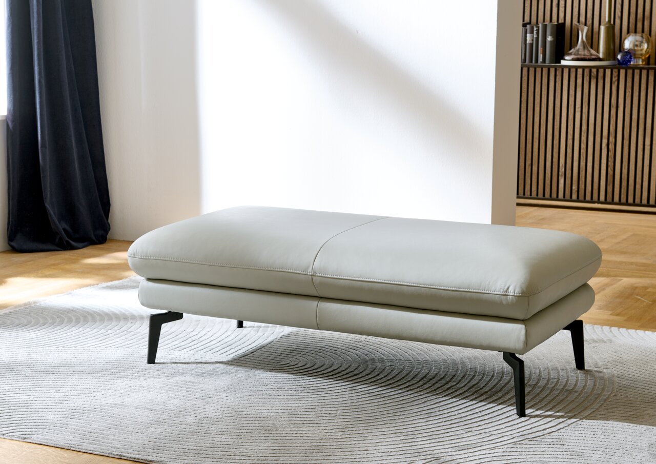 Dieter Knoll XXL-Hocker ARZONA L XXL-Hocker in hellgrauem Leder, seitliche Perspektive, auf einem gemusterten Teppich stehend.