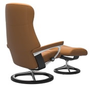 Achterkant van een bruine Stressless-eenpersoonsfauteuil met voetenbankje, modern ontwerp met details van metaal en hout.