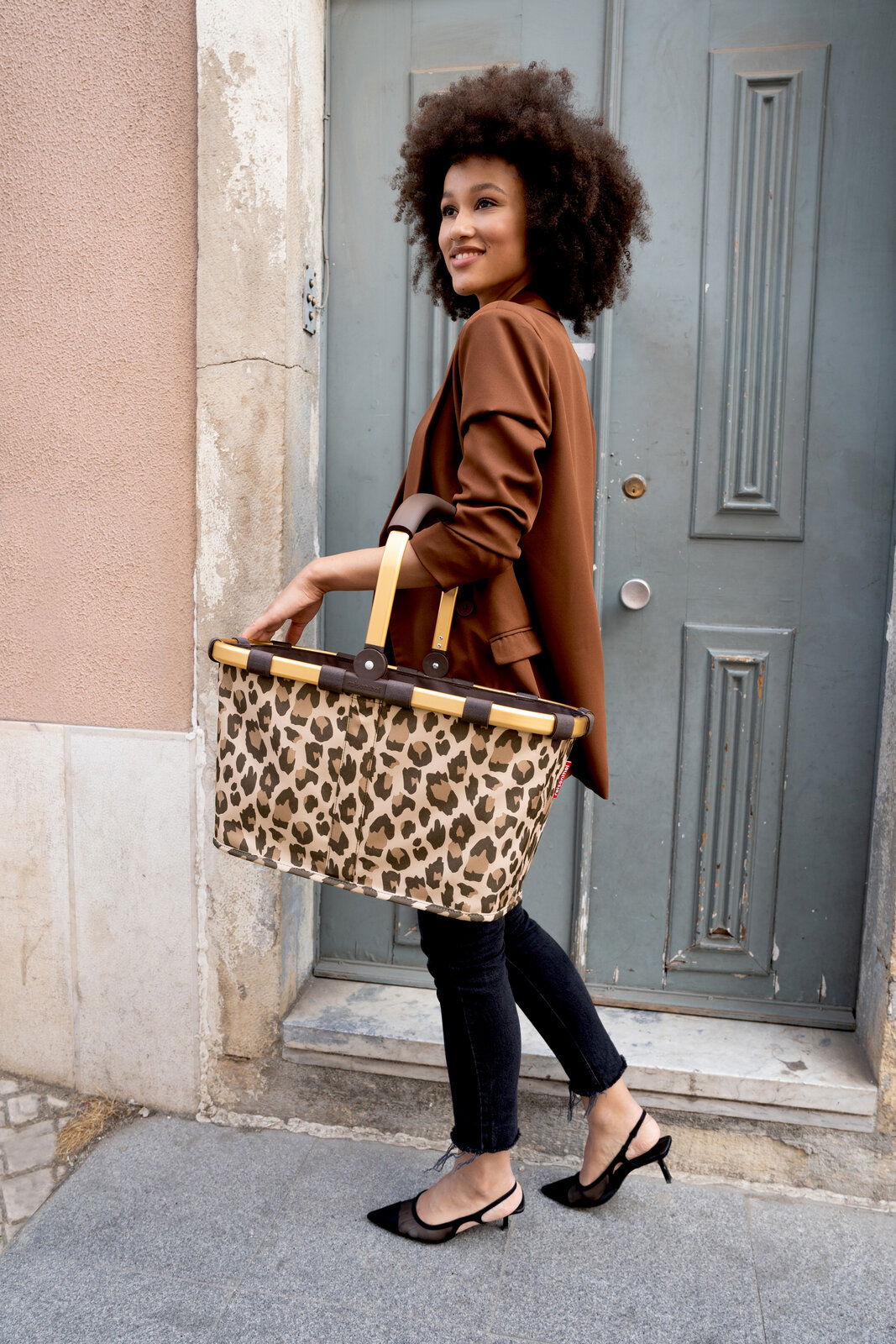 Reisenthel Carrybag FRAME LEO MACCHIATO Frau mit braunem Blazer trägt einen Carrybag mit Leopardenmuster, seitliche Perspektive