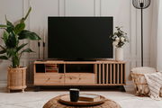 Frontale Ansicht eines stilvollen TV-Lowboards aus Holz mit dekorativen Elementen, einem großen Fernseher darauf und Pflanzen sowie Dekorationen daneben.