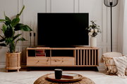 Frontale Ansicht eines stilvollen TV-Lowboards aus Holz mit dekorativen Elementen, einem großen Fernseher darauf und Pflanzen sowie Dekorationen daneben.