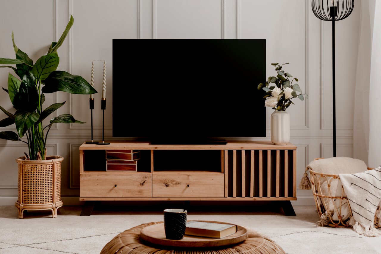 Frontale Ansicht eines stilvollen TV-Lowboards aus Holz mit dekorativen Elementen, einem großen Fernseher darauf und Pflanzen sowie Dekorationen daneben.