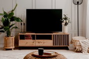 Frontale Ansicht eines stilvollen TV-Lowboards aus Holz mit dekorativen Elementen, einem großen Fernseher darauf und Pflanzen sowie Dekorationen daneben.