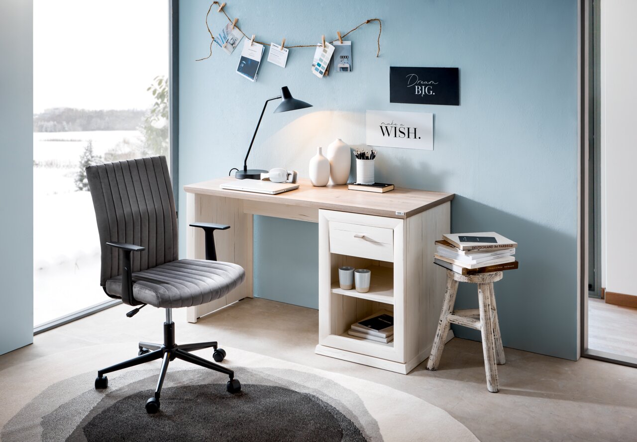 Moderner Schreibtisch in heller Holzoptik mit Schublade und Regal, seitliche Perspektive, dekoriert mit Lampe, Vasen und Büchern, neben einem großen Fenster mit Blick auf eine verschneite Landschaft.