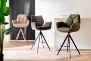 Drei moderne Barstühle in verschiedenen Farben und Materialien, von links nach rechts: beige Stoff, grauer Stoff und grünes Leder, auf einem hellen Holzboden vor einer weißen und dunklen Wand. Perspektive: Frontalansicht.