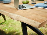 Nahaufnahme eines Esstisches aus Holz mit natürlicher Kante, darauf ein Laptop und grüne Äpfel, im Freien aufgestellt.