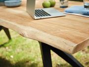 Nahaufnahme eines Esstisches aus Holz mit natürlicher Kante, darauf ein Laptop und grüne Äpfel, im Freien aufgestellt.